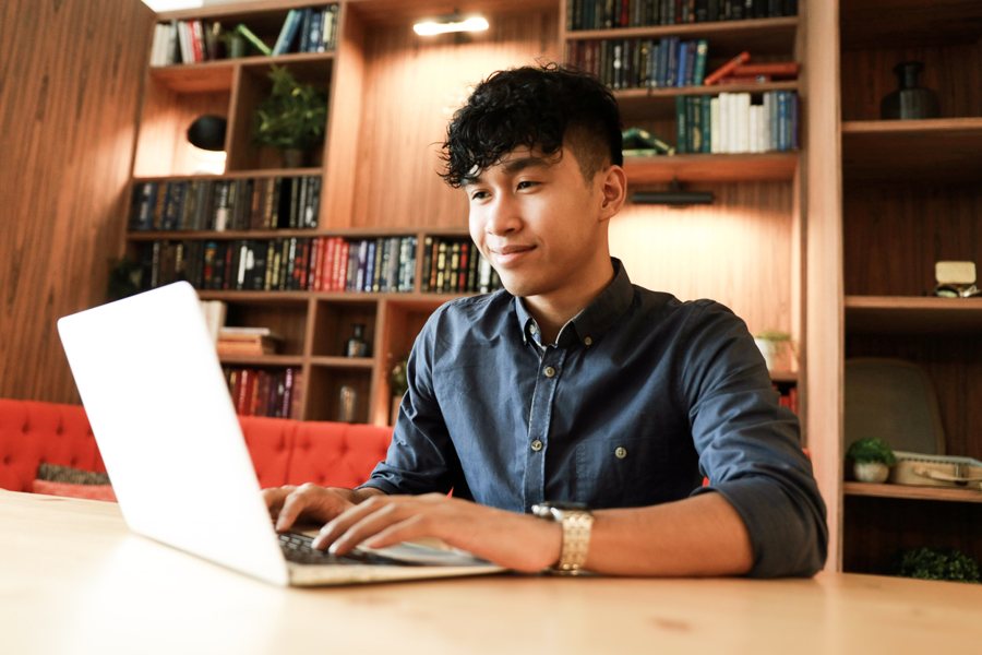 A student smiling while working on a laptop in a library