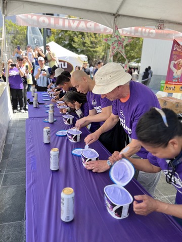 Contestants in purple shirts racing through cups of ice cream at a festival culinary pavilion
